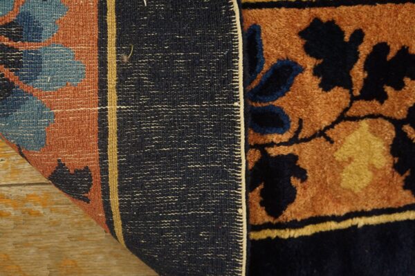 The edge of a floral brown and navy high-pile rug is folded over, revealing the woven back on wood.