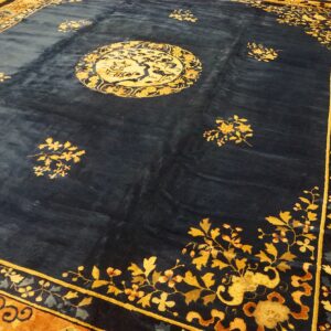 Navy field rug with a gold medallion and rust-colored floral borders on a wood floor.