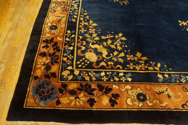 Dark navy rug with gold floral patterns and a wide rust-colored border on a wooden floor.
