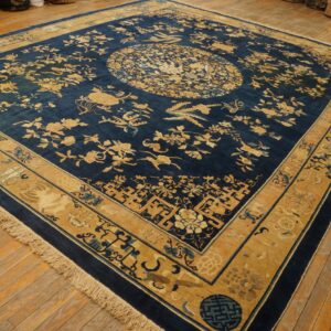Indigo rug with gold and tan botanical patterns, a central medallion, and fringes on wood flooring.