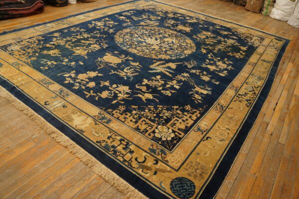 Indigo rug with gold and tan botanical patterns, a central medallion, and fringes on wood flooring.
