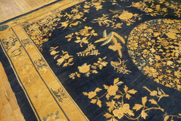 Detailed navy blue rug with contrasting gold floral and bird designs rests on light wood floor.