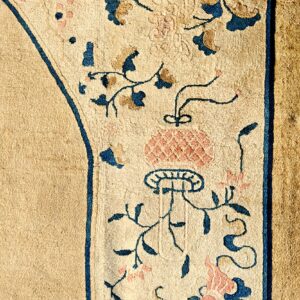 Close-up of low-pile tan rug with a border featuring scrolling blue and pink botanical designs.