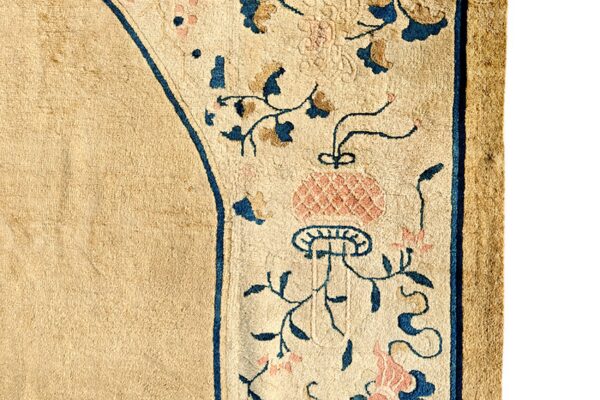 Close-up of low-pile tan rug with a border featuring scrolling blue and pink botanical designs.