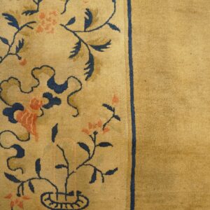 Detail of a gold rug showing a thick navy-lined border with coral flowers and blue scrolling leaves.