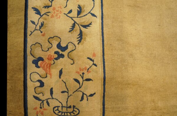 Detail of a gold rug showing a thick navy-lined border with coral flowers and blue scrolling leaves.