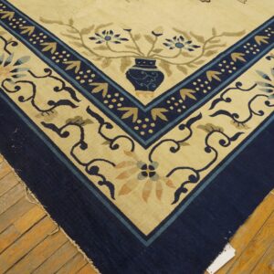 Cream and navy rug corner featuring stylized vase and floral patterns rests on worn wood flooring.