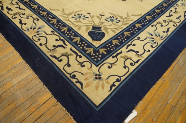 Cream and navy rug corner featuring stylized vase and floral patterns rests on worn wood flooring.