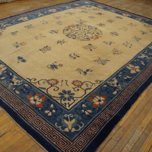 Cream field rug with scattered florals and a wide blue border on distressed yellow wooden floors.