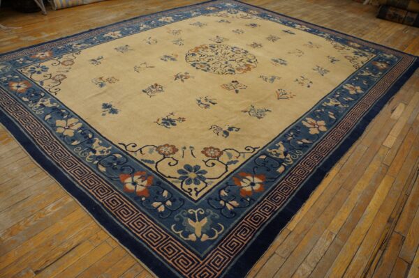 Cream field rug with scattered florals and a wide blue border on distressed yellow wooden floors.