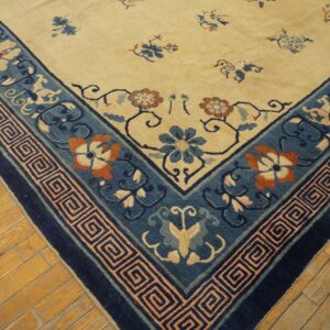 Cream rug corner with blue, orange, and pink floral patterns and a geometric border on distressed wood flooring.