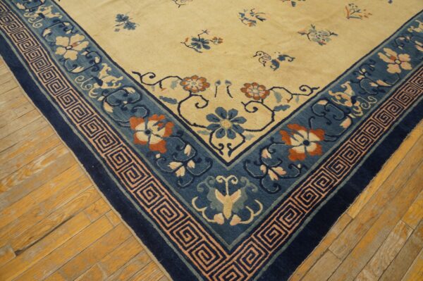 Cream rug corner with blue, orange, and pink floral patterns and a geometric border on distressed wood flooring.