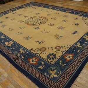Large tan rug with scattered floral motifs and a wide navy blue patterned border on wood flooring.