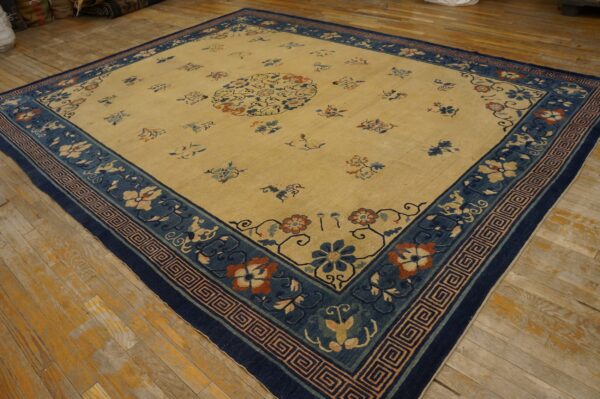 Large tan rug with scattered floral motifs and a wide navy blue patterned border on wood flooring.