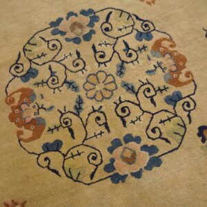 Low-pile tan rug featuring a large circular motif with blue, rust, and rose colored floral designs.