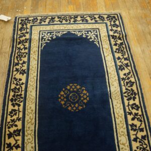 Blue niche-shaped rug with cream and gold floral borders laid on distressed light wood floors.