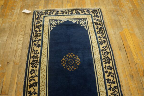 Blue niche-shaped rug with cream and gold floral borders laid on distressed light wood floors.