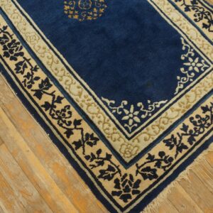 Blue rug with contrasting cream and navy stylized floral borders rests on rustic plank wood flooring.