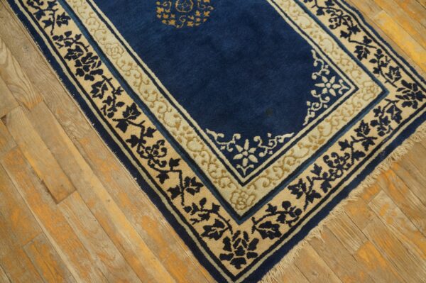 Blue rug with contrasting cream and navy stylized floral borders rests on rustic plank wood flooring.