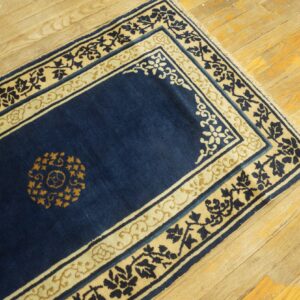 Navy blue rug runner with contrasting cream and gold floral borders on light, distressed wood plank flooring.