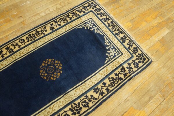 Navy blue rug runner with contrasting cream and gold floral borders on light, distressed wood plank flooring.