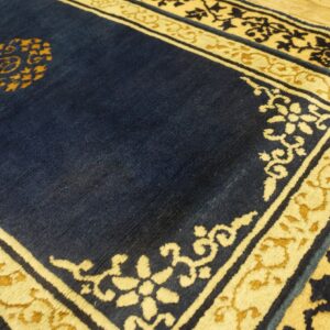 Close-up of a navy blue rug with cream and gold borders and a central medallion on wood flooring.