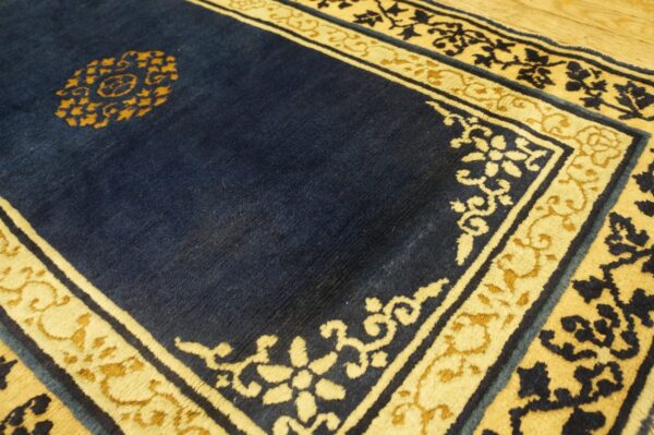 Close-up of a navy blue rug with cream and gold borders and a central medallion on wood flooring.