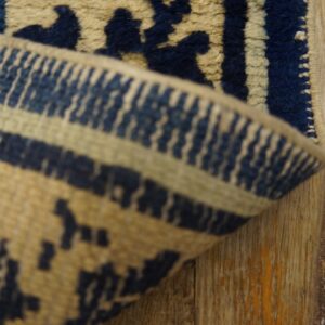 Close-up of a deep blue and beige patterned rug border folded on rustic wood planks.