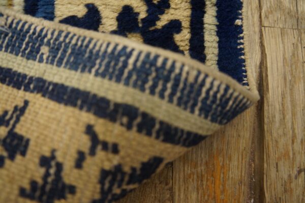 Close-up of a deep blue and beige patterned rug border folded on rustic wood planks.