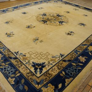 A large yellow rug with a navy blue and gold floral border is displayed on distressed wood flooring.
