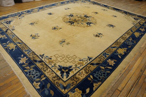 A large yellow rug with a navy blue and gold floral border is displayed on distressed wood flooring.