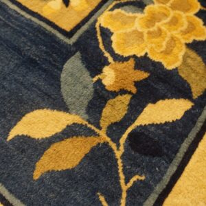 Dark blue rug detail with bold yellow and brown floral elements and a wide gold border.
