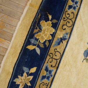 The cream rug border has navy blue and tan floral bands against light brown wooden floorboards.