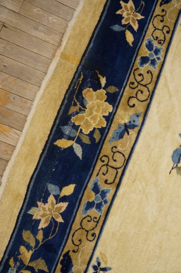 The cream rug border has navy blue and tan floral bands against light brown wooden floorboards.