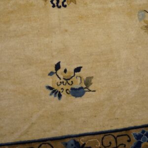 Tan high-pile rug with scattered blue and gold floral designs and a patterned blue and brown border.