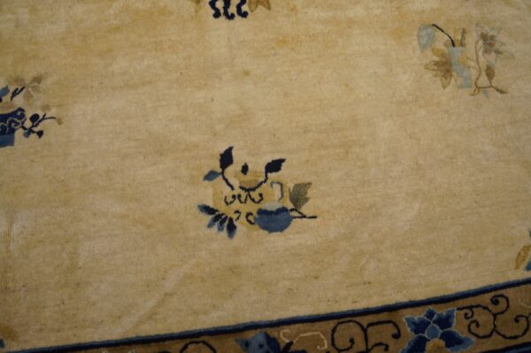 Tan high-pile rug with scattered blue and gold floral designs and a patterned blue and brown border.