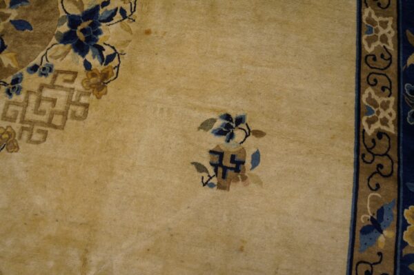Detail of a medium pile tan rug with floral and geometric patterns in navy, light blue, and gold tones.