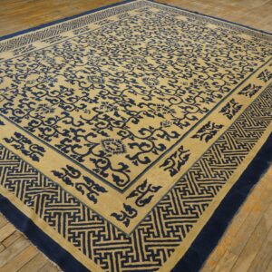 Tan and navy rug featuring a vine pattern and thick geometric border lying on distressed wood floor.