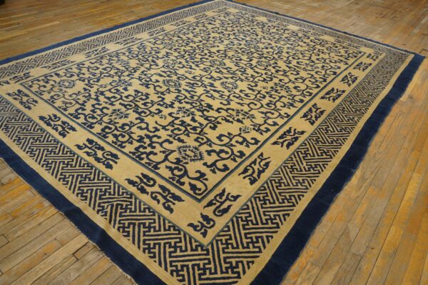 Tan and navy rug featuring a vine pattern and thick geometric border lying on distressed wood floor.