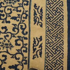 Close-up of a blue and tan rug displaying floral and geometric borders on wood floor.