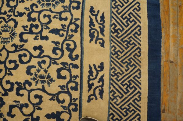 Close-up of a blue and tan rug displaying floral and geometric borders on wood floor.