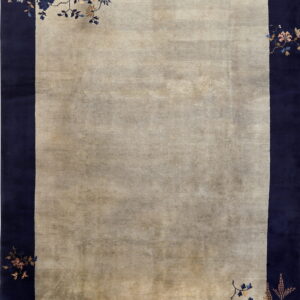 Muted beige rug with a wide navy blue border and delicate floral vine motifs in the corners.