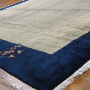 Low-pile beige and navy rug with a floral border accent lying on worn wood planks.
