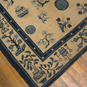A tan rug featuring detailed blue floral and symbolic motifs, bordered by dark blue bands, resting on hardwood floors.