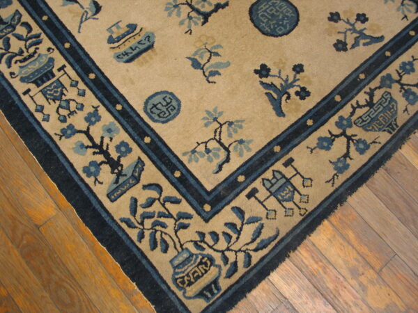 A tan rug featuring detailed blue floral and symbolic motifs, bordered by dark blue bands, resting on hardwood floors.