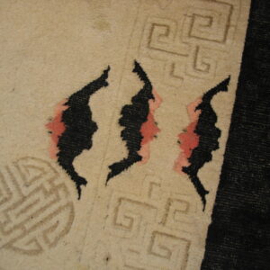 Tan rug close-up showing black abstract designs with pink accents and light brown linear geometric patterns.