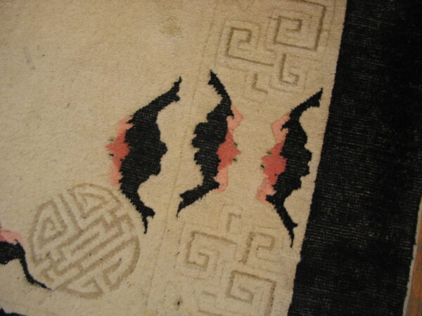 Tan rug close-up showing black abstract designs with pink accents and light brown linear geometric patterns.