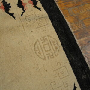 Beige rug with black and pink details and subtle geometric shapes rests on distressed wood planks.