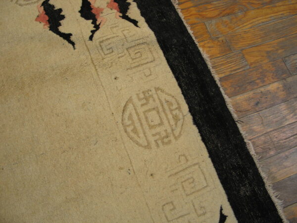 Beige rug with black and pink details and subtle geometric shapes rests on distressed wood planks.