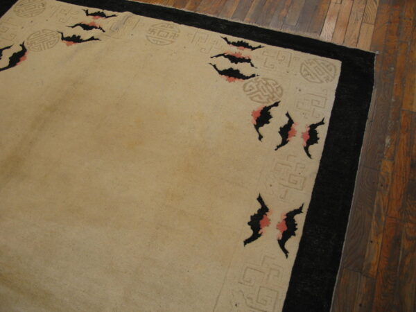 Tan rug featuring a black border, light fretwork, and black and pink bat motifs on wood planks.